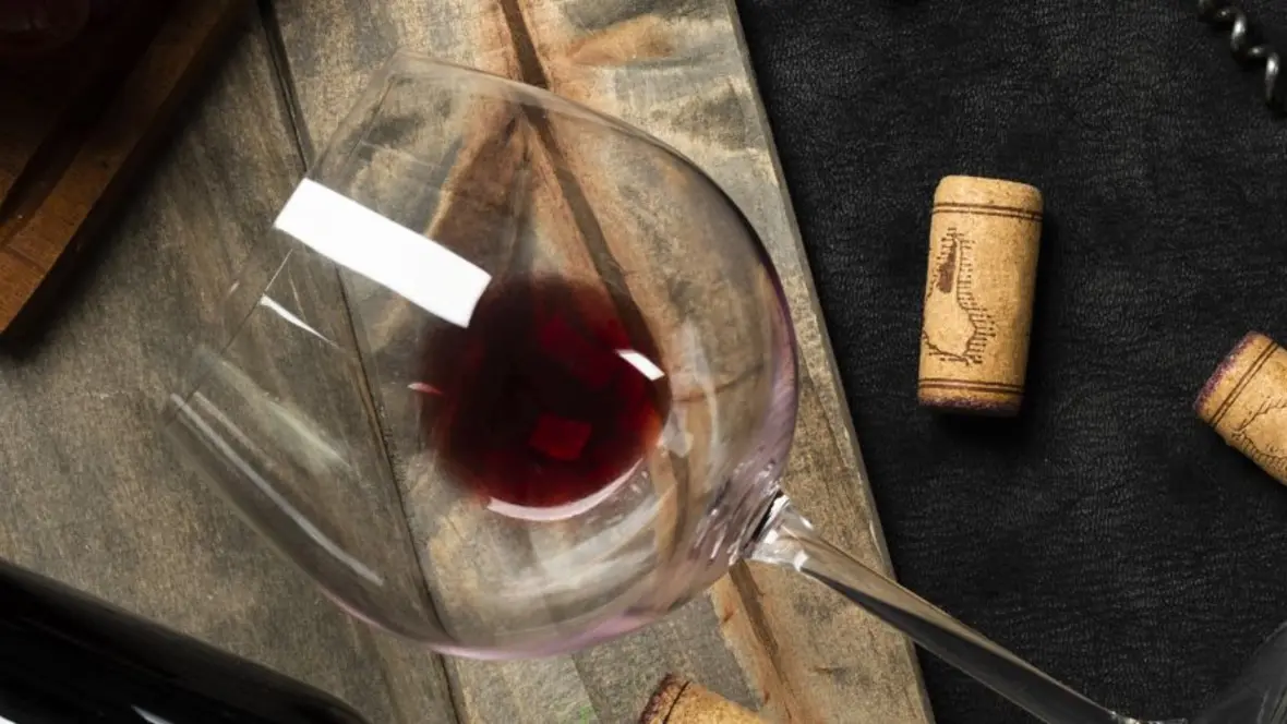 Weinglas auf Holz mit Korken Liegendes Weinglas mit etwas Rotwein auf Holz mit Korken.